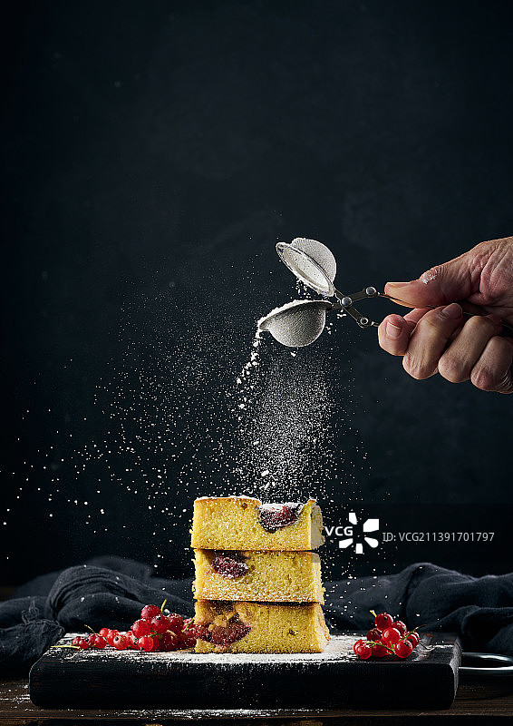 在蛋糕上撒糖粉的手部，黑色背景图片素材