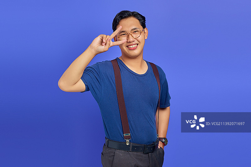 在紫色背景前比出“V”字手势的快乐亚洲男人，印度尼西亚图片素材