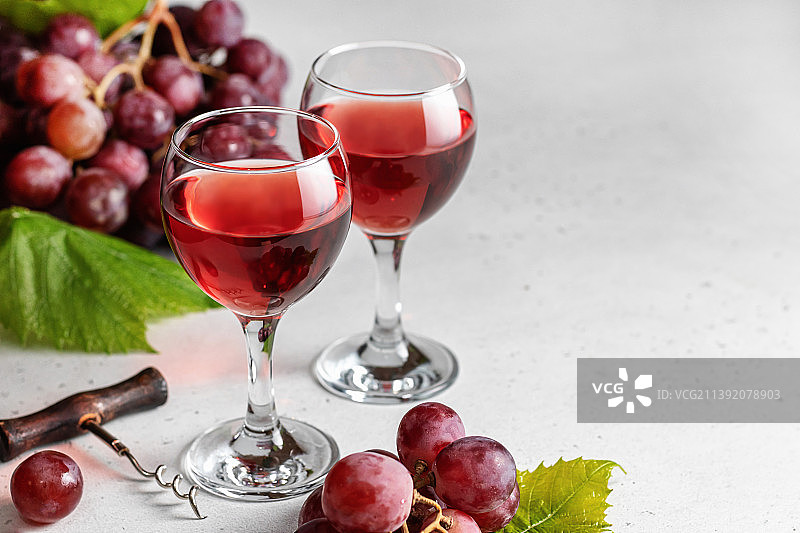 两杯红酒、葡萄和开瓶器，浅色背景留白图片素材