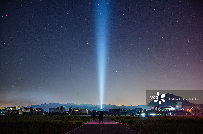 乡村星空下的稻田，一个人拿着手电筒照射。图片素材