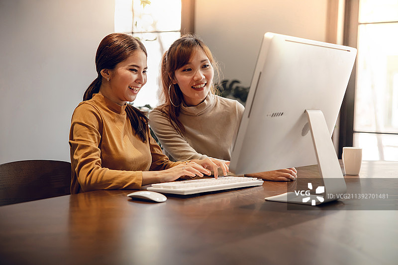 团队合作，共同努力微笑的两名商务女性在泰国使用电脑工作图片素材