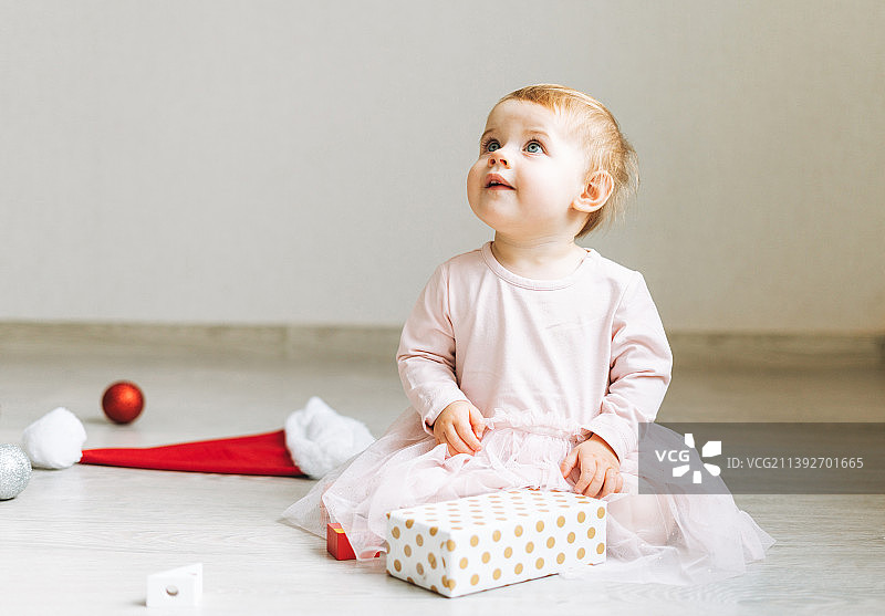穿着粉色连衣裙，房间地板上放着礼品盒的可爱女婴图片素材