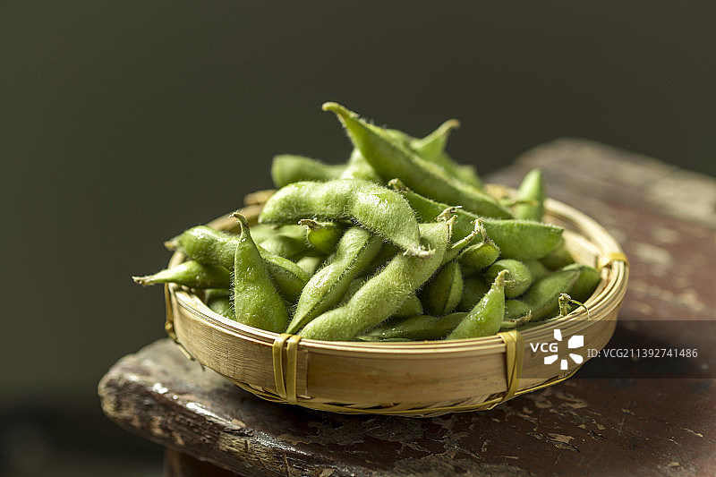 一簸箕毛豆角摆放在木桌面上特写深色调图片素材
