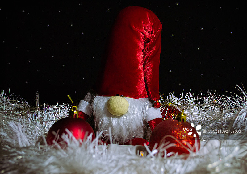 有趣的玩具新年小矮人，戴着红色帽子，周围是红色圣诞玩具和白色金属丝，德国图片素材