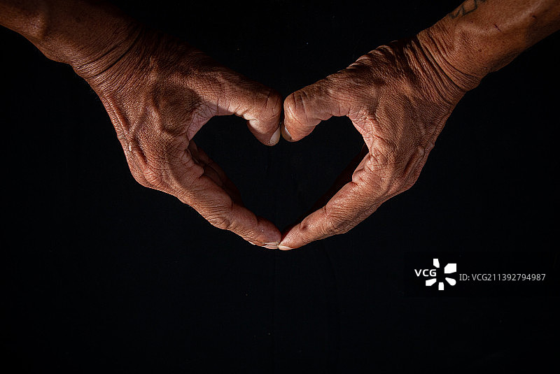 男人在黑色背景下用手做出心形的特写镜头图片素材
