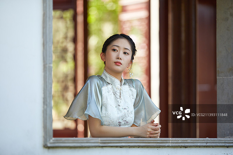 身穿旗袍站在窗边的年轻女孩图片素材