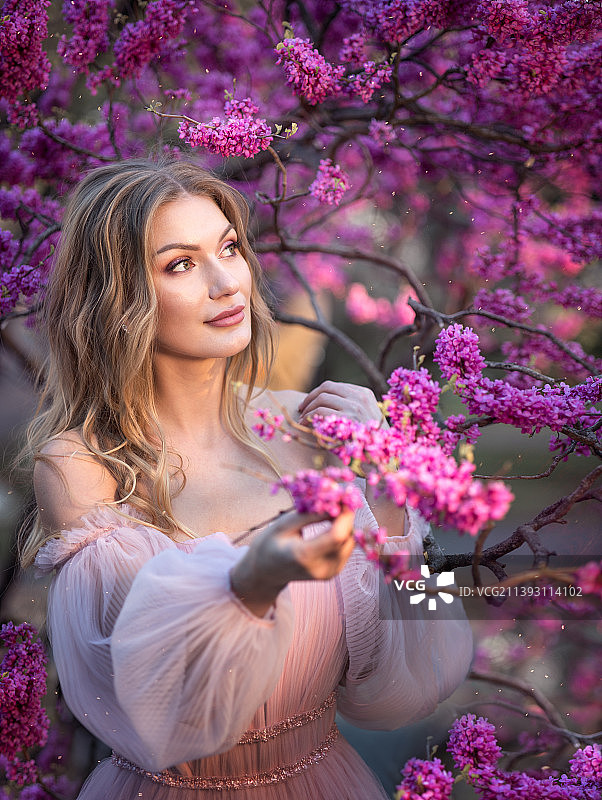 身穿飘逸连衣裙站在粉色鲜花树旁的俄罗斯美女图片素材