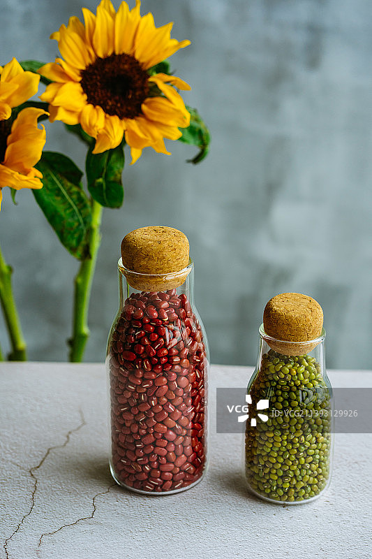玻璃瓶装的红豆和绿豆，摆放在素净的大理石桌上图片素材