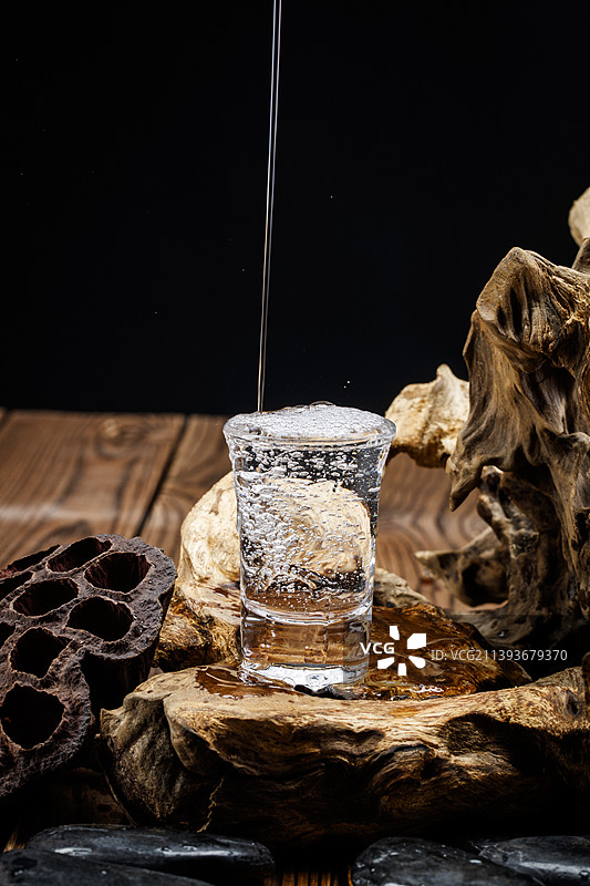 向木板上摆放的酒具内倒入清澈的白酒酒花图片素材