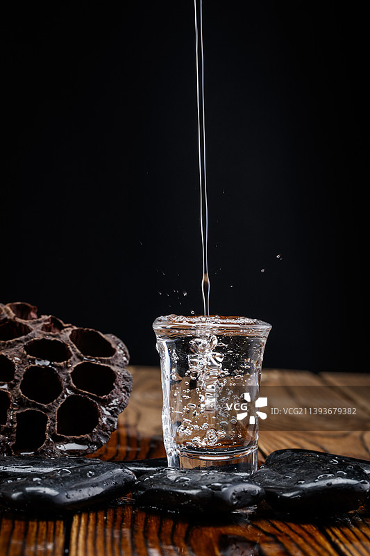 向木板上摆放的酒具内倒入清澈的白酒酒花图片素材