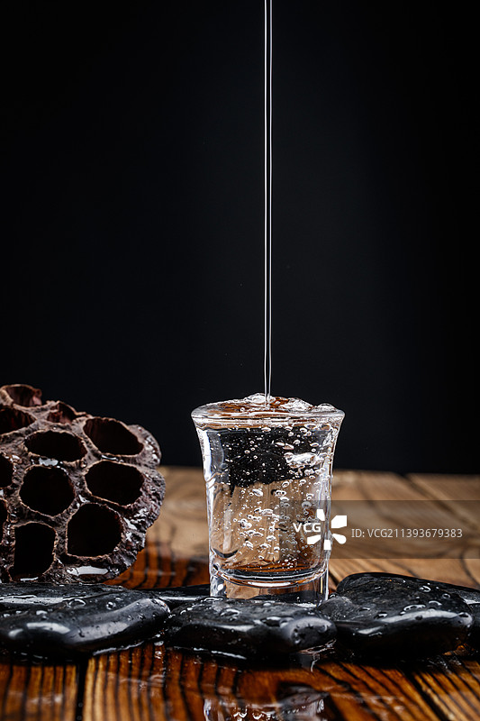 向木板上摆放的酒具内倒入清澈的白酒酒花图片素材