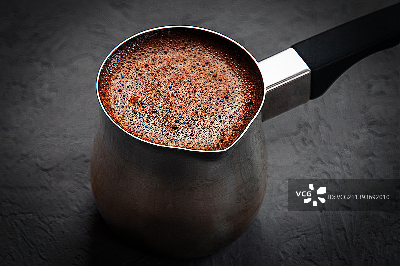 深灰色背景下用土耳其咖啡壶冲泡的棕色泡沫咖啡图片素材