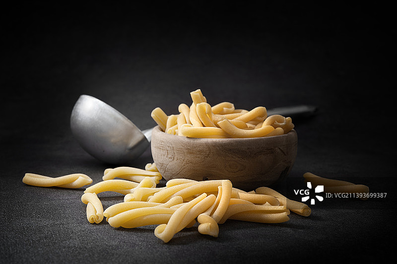 深灰色背景下木碗里的卡萨雷切意大利面和勺子，留白图片素材