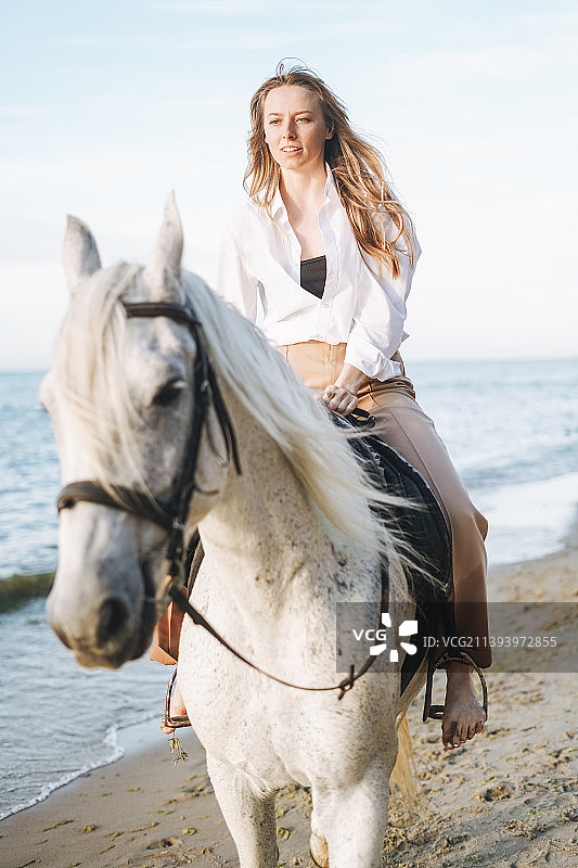年轻长发女人白衬衫骑白马海景背景图片素材