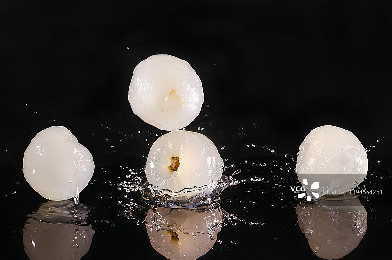 黑色背景下几颗剥皮后的乳白色爆汁荔枝果实溅起透明水花图片素材
