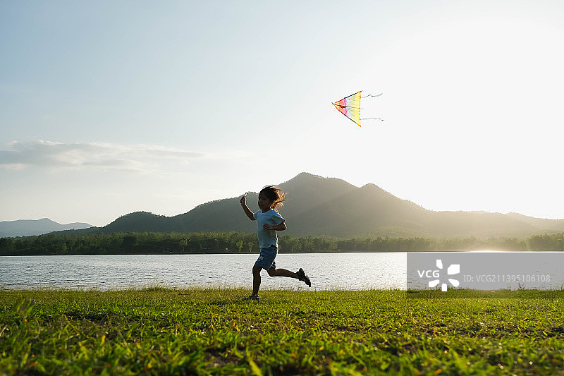 孩子们在泰国日落时分在湖边草地上放风筝图片素材