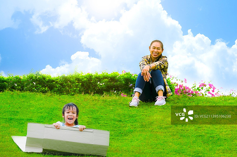 在泰国植物园坐在纸板箱上滑下山坡的微笑小女孩图片素材