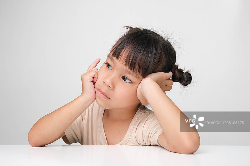 在粉色背景的桌旁快乐微笑的可爱深色头发女孩图片素材