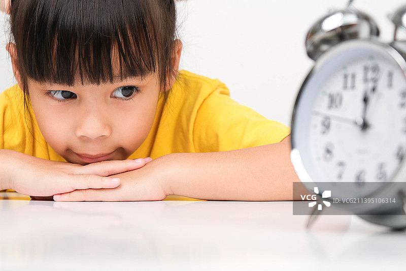 可爱的黑发女孩手托下巴看着复古闹钟，泰国图片素材