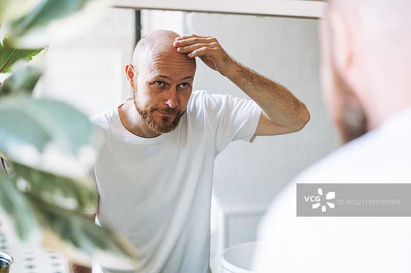 在浴室照镜子，担心脱发的年轻络腮胡男子图片素材