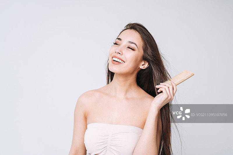 在白色背景下用木梳梳理黑色长发的亚洲女人图片素材