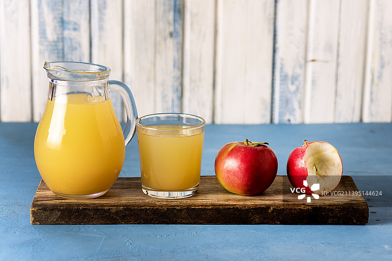 蓝色背景木制托盘上的玻璃壶和玻璃杯中的鲜榨苹果汁图片素材