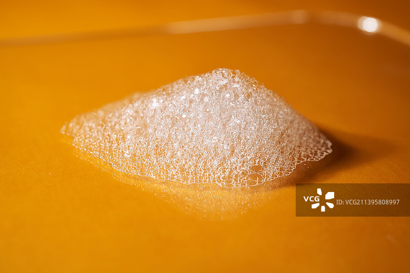 明亮黄色背景上的洗发水或沐浴露产生的白色泡沫图片素材