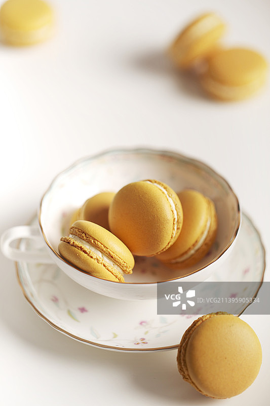一组马卡龙图片 美食摄影 亮色调名色调 红茶杯里装满柠檬味黄色马卡龙甜品 夹心图片素材