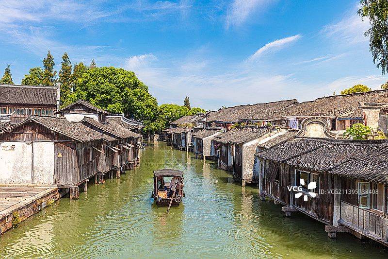 浙江嘉兴桐乡乌镇东栅水乡全景，盛夏的蓝天白云，乌篷船慢慢摇摆，行驶在东市河上，两岸都是木结构传统民居图片素材