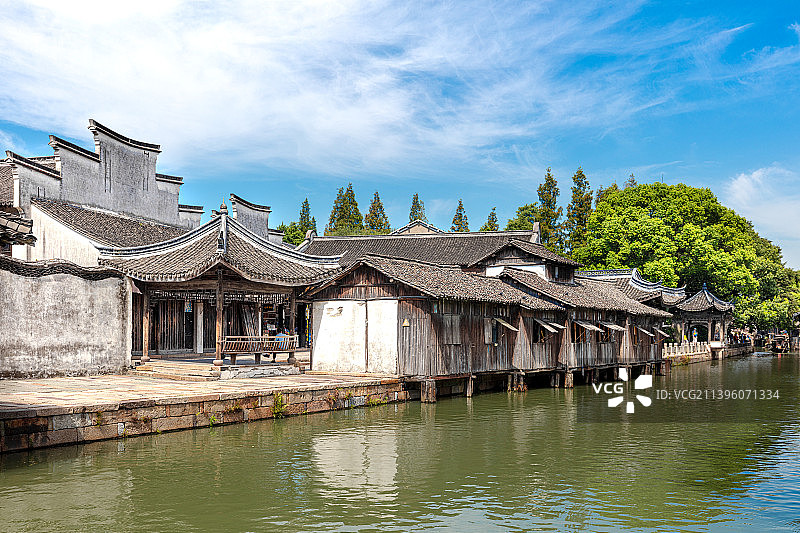 嘉兴桐乡乌镇东栅沿河徽派民居白墙黛瓦马头墙，木板窗扇扇打开，四角方亭坐着休息的路人，古典水乡园林风光图片素材