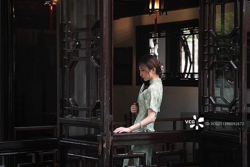 身穿旗袍手持雨伞古典书籍圆扇在庭院园林里散步的古典美女图片素材