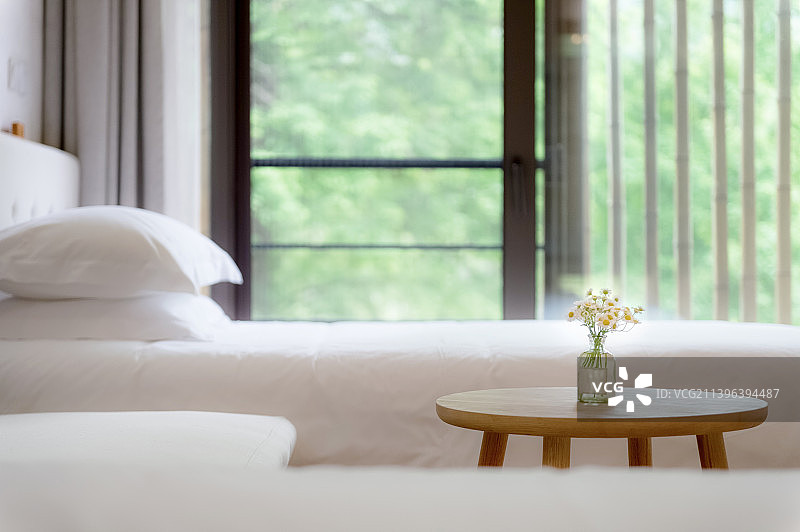 床头插花和白色床铺枕头在绿色窗前图片素材