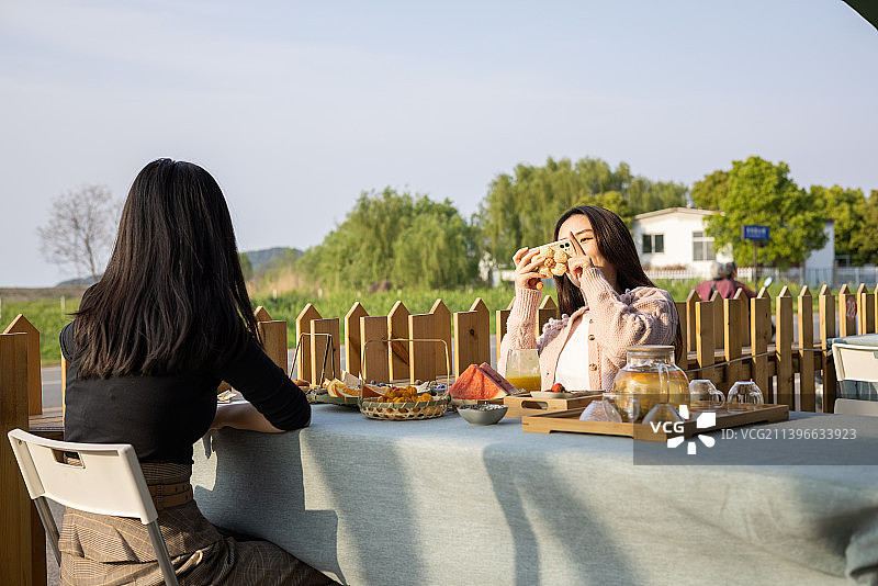 春季夕阳下两个年轻女孩社交聚会喝下午茶吃点心聊天拍照片图片素材