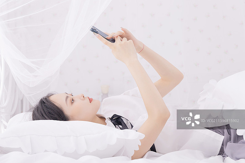 躺在床上玩手机的年轻女性图片素材