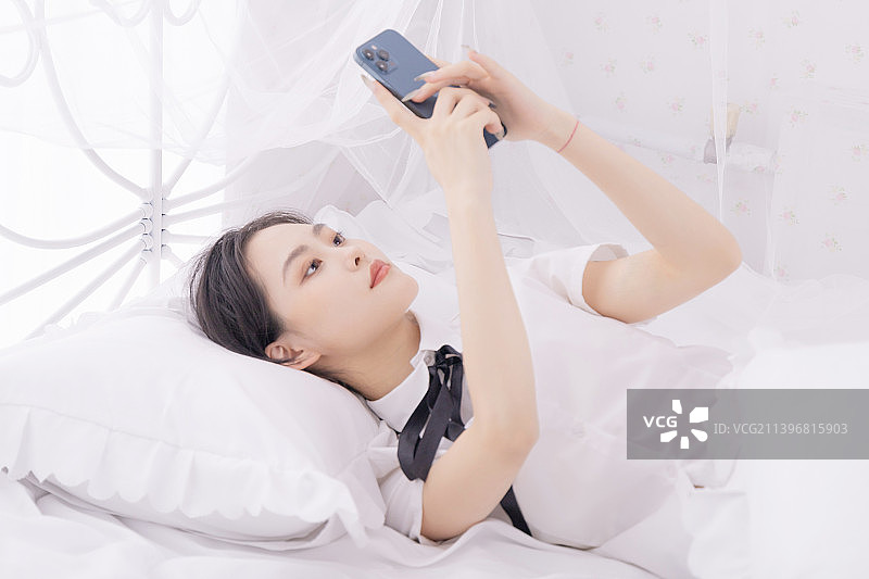 躺在床上玩手机的年轻女性图片素材