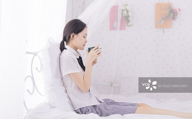 年轻女子坐在家里的床上喝水图片素材