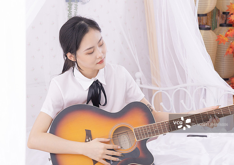 床上弹吉他的年轻女性图片素材