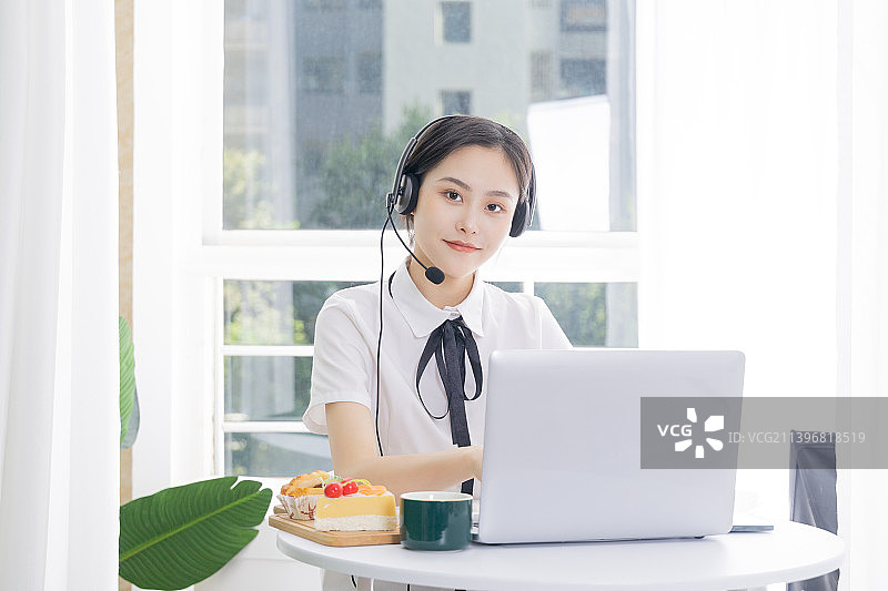 戴着耳机的年轻女子在办公室用笔记本电脑工作图片素材