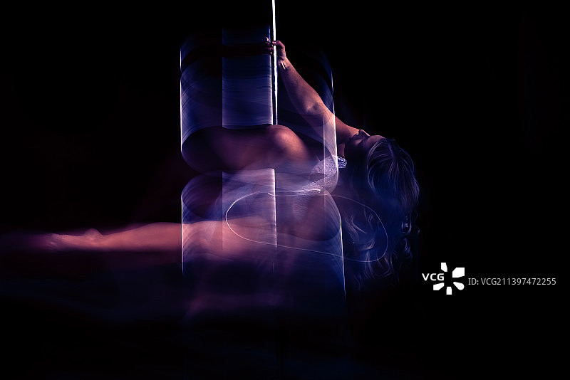 长曝光：黑背景下在钢管上跳舞的女人特写，加拿大艾伯塔省埃德蒙顿图片素材