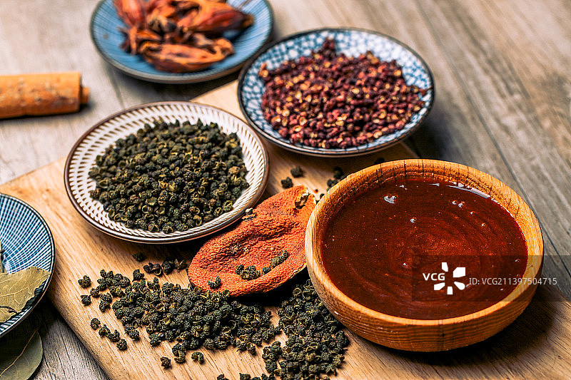 浅色木板上放着几个碗碟，里面分别装着青花椒、红花椒、八角香料、香油图片素材