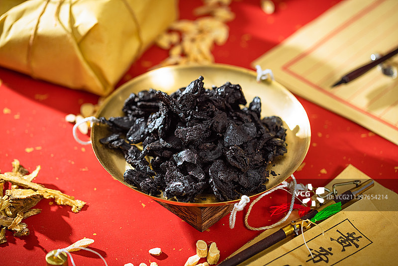 放在金色秤盘子里的中药熟地黄，本子上写的汉字是“黄帝内经”图片素材