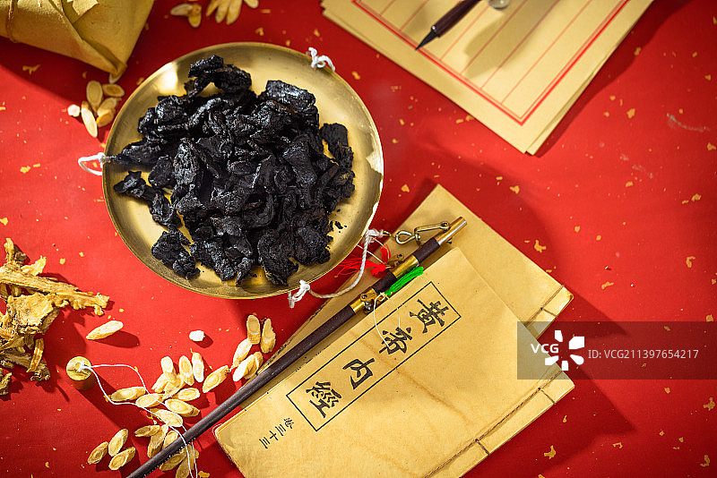 放在金色秤盘子里的中药熟地黄，本子上写的汉字是“黄帝内经”图片素材
