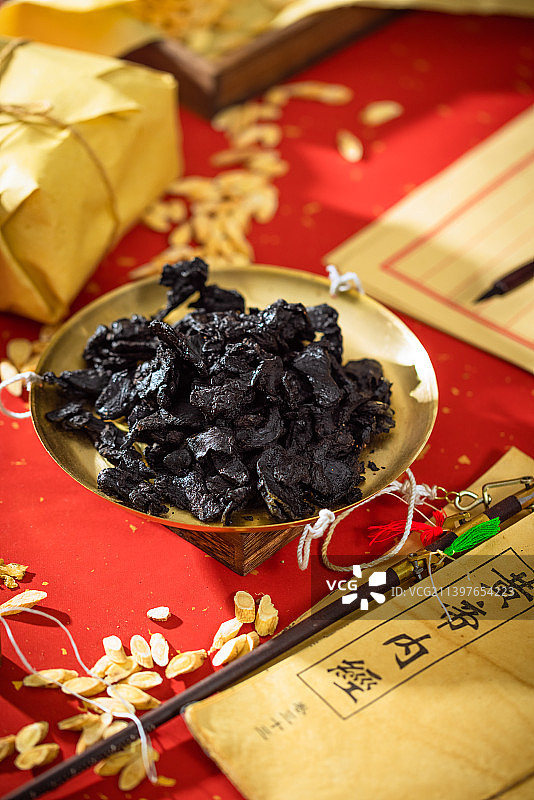 放在金色秤盘子里的中药熟地黄，本子上写的汉字是“黄帝内经”图片素材