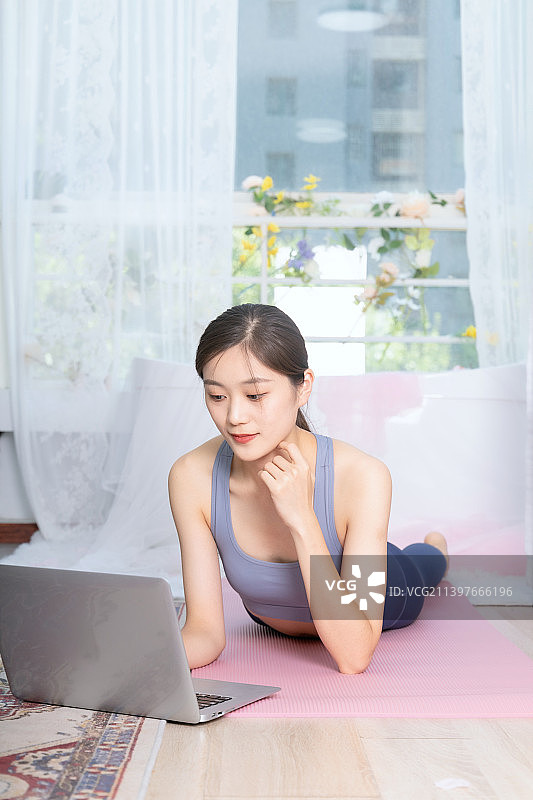 年轻女子在家运动垫上使用笔记本电脑图片素材