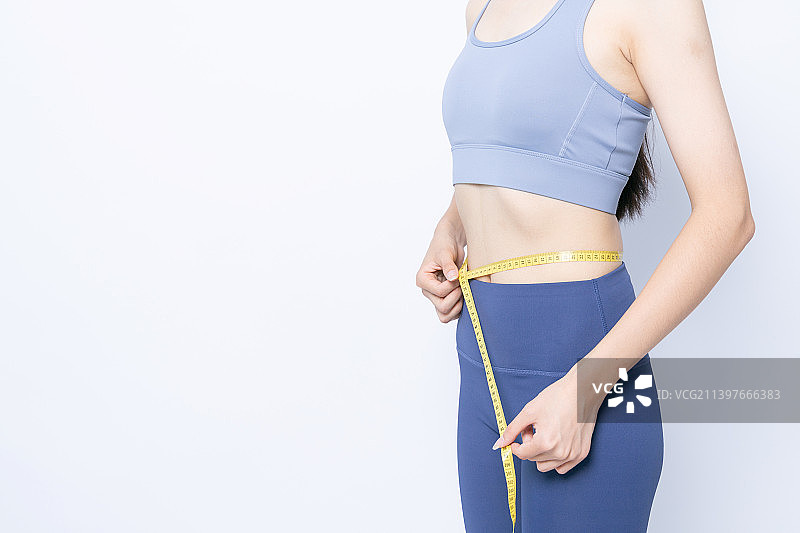 白色背景前测量腰围的运动内衣女性图片素材