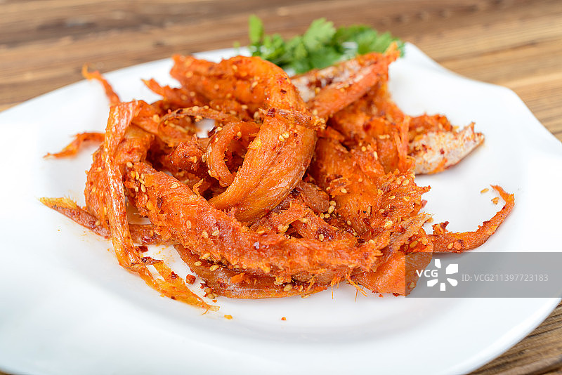 木纹桌上白瓷盘中的辣拌明太鱼丝图片素材