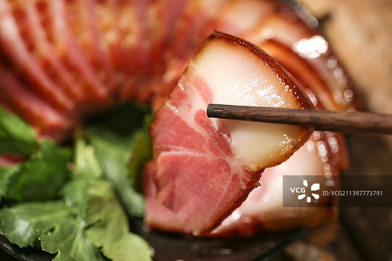 整齐摆放腊肉片的盘子上方用黑色筷子夹着一片肥瘦均匀的腊肉图片素材