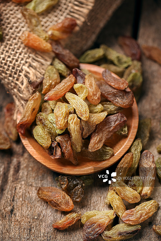 浅色木纹背景里摆着一个盛满葡萄干的木碟子且旁边散落着些葡萄干图片素材