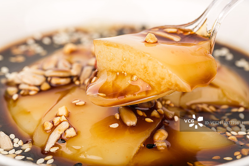 洒满花生碎和白芝麻的红糖凉糕上用勺子舀了一块凉糕图片素材