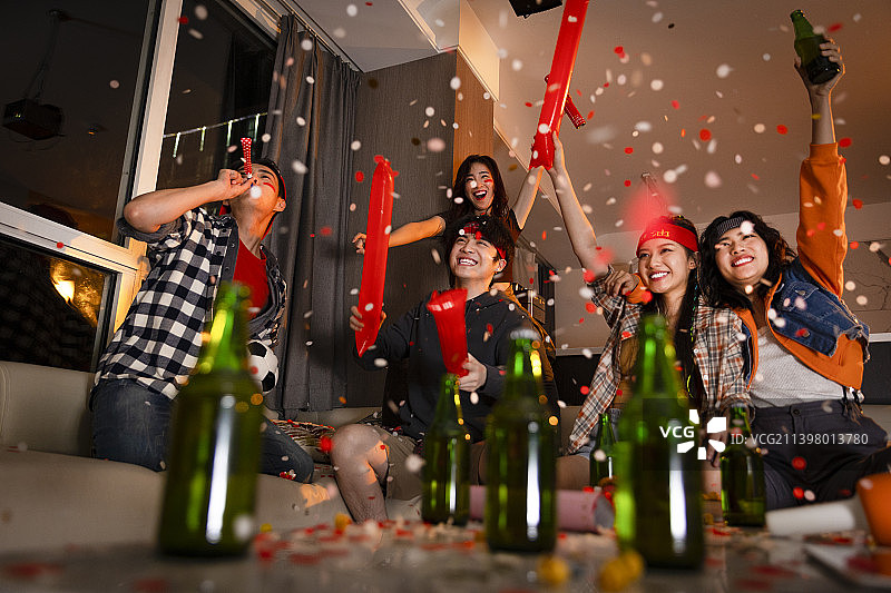 快乐的年轻人在客厅观看足球比赛:欢呼呐喊庆祝胜利图片素材